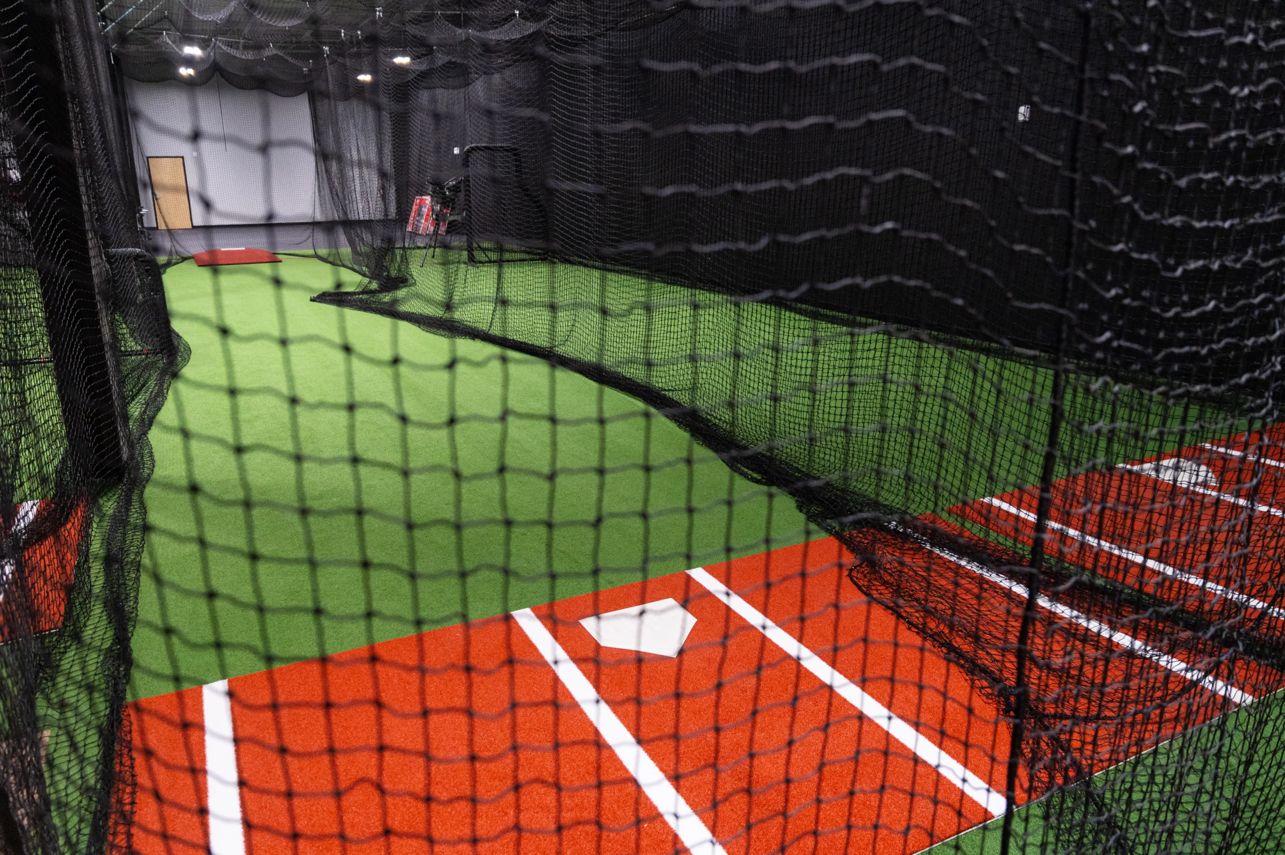 Batting cage tunnel with turf and a clay batting mat and home plate, seen through the netting