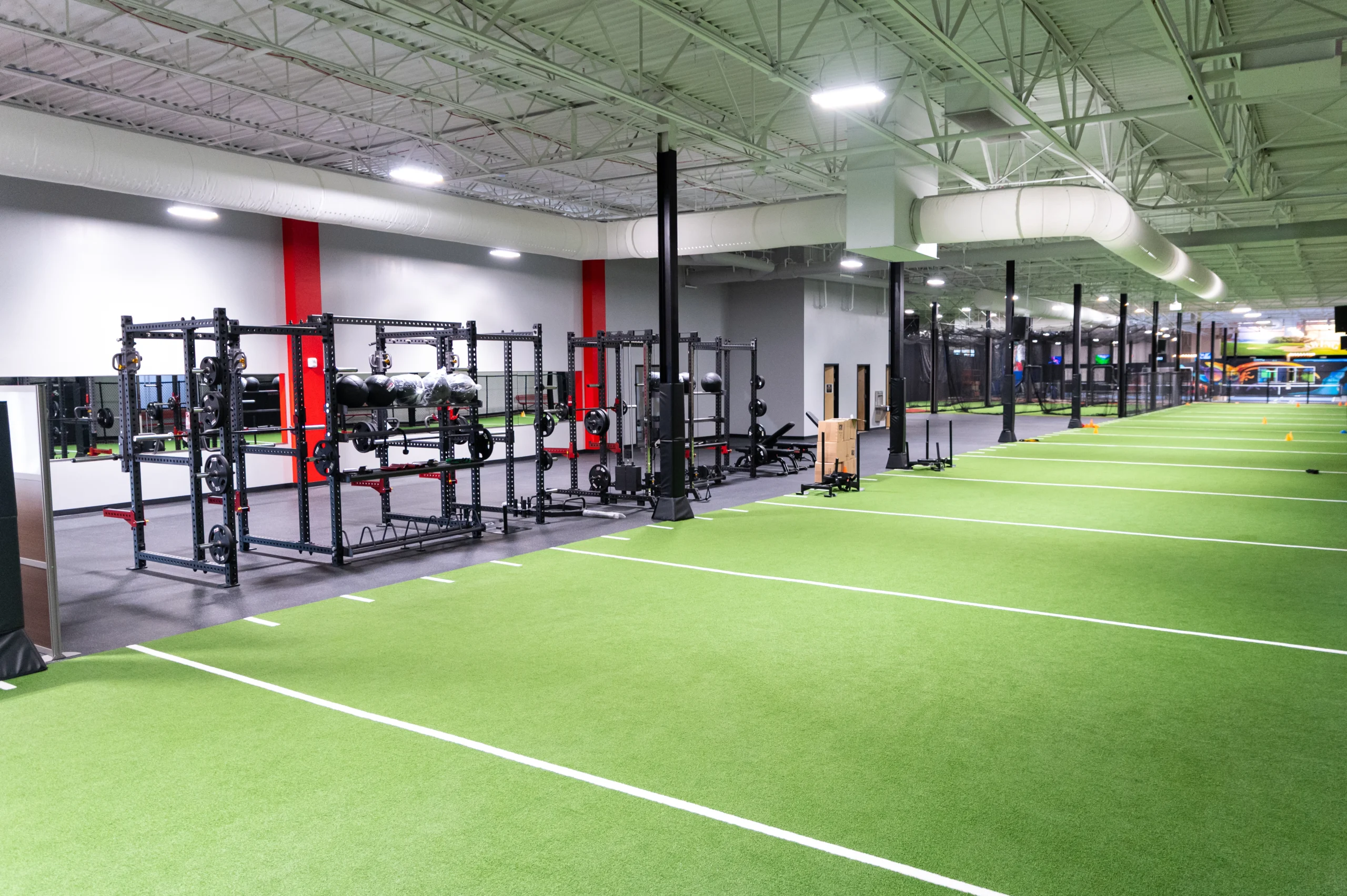 Squat racks and barbells lining the strength area next to the turf sprint lanes